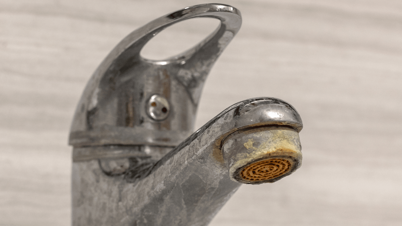 Faucet with visible hard water build up and calcium deposits, showing mineral buildup, limescale, and soap scum around the aerator. The image illustrates how to remove hard water build up on metal fixtures caused by dissolved minerals like calcium carbonate and magnesium. Common in industrial water systems, this buildup reduces water flow and efficiency, requiring cleaning solutions such as vinegar and baking soda or professional descaling methods.