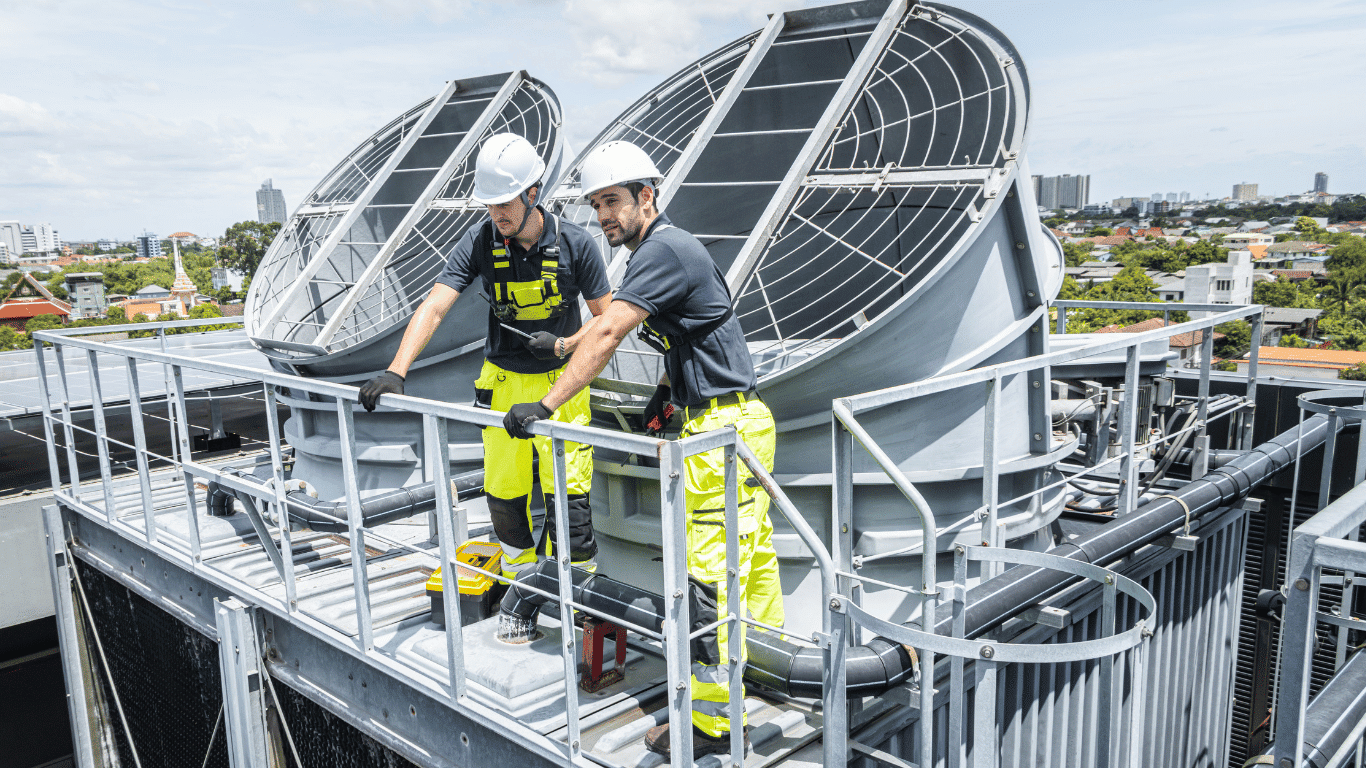 Technicians wearing personal protective equipment inspect and clean cooling towers on a rooftop as part of cooling tower maintenance for an HVAC system in a manufacturing facility, focusing on the cooling tower basin to remove dirt, scale, and algae that can lead to legionella. Regular tower maintenance helps facility managers disinfect and apply biocides to the fill and other components, ensuring cooling towers operate efficiently with optimal performance and peak efficiency. Proper disinfection and safety procedures during cooling tower maintenance improve HVAC effectiveness, keep energy costs and operational cost at a minimum, and provide crucial benefits for reliable cooling and long-term HVAC system efficiency.