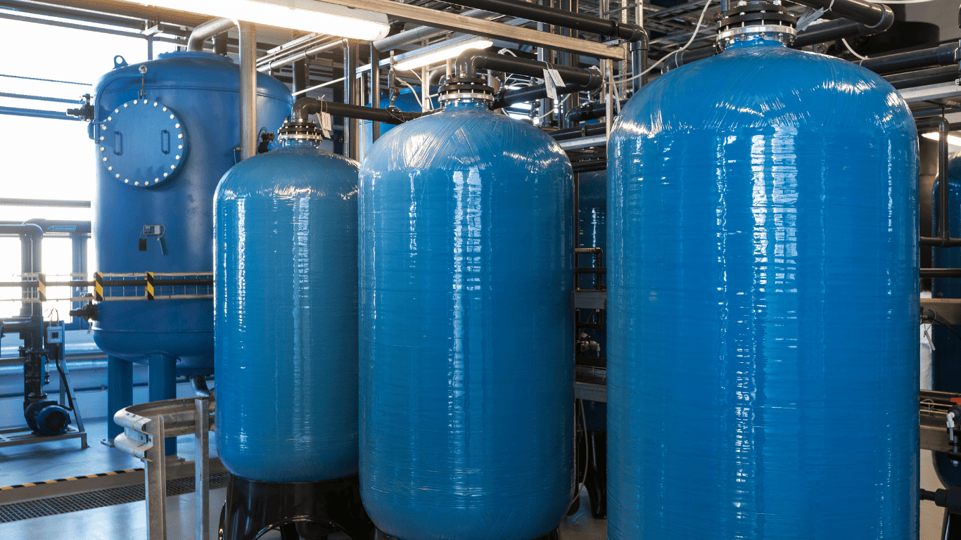Industrial water softener system in a commercial and industrial water treatment facility showing large blue tank units with engineered valves and plumbing designed for high flow rate water systems used in industrial applications, boiler systems, and institutional applications to convert hard water into soft water through filtration, filters, reverse osmosis integration, and salt-based water softener processes for better tasting water and reliable water treatment systems. Commercial water softener and industrial water softener equipment installed as part of advanced commercial water softener systems in commercial and industrial facilities, featuring multiple tank vessels, automated valves, and high-capacity filtration filters that remove iron, copper, and other minerals from hard water to produce soft water for industries, appliances, and large water systems requiring efficient water treatment. Large-scale industrial water softener tank installation with engineered valves and plumbing connected to water treatment systems that manage high flow rate gallons of water for commercial and industrial industries, supporting boiler systems and institutional applications while preventing mineral drop and scaling from hard water through filtration, filters, chemicals, and salt treatment solution technology. Commercial water softener systems and industrial water softener units operating in a water treatment plant with a full line of water treatment and filtration equipment including reverse osmosis systems, filters, and softener tanks designed for commercial and industrial applications where reliability, energy efficiency, and high quantity water flow rate make a big difference for customers across many industries. Industrial water softener and commercial water softener system with blue tank vessels and advanced valves engineered for water systems that treat hard water with salt and chemicals to reduce iron, copper, and alkalinity levels, improving plumbing performance, protecting appliances, and delivering soft water in commercial, industrial, and limited residential water treatment installations. Commercial and industrial water treatment systems including industrial water softener equipment, reverse osmosis filtration, and multiple filters working together as a complete water treatment solution engineered for high flow rate gallons of water, helping industries and customers maintain reliable boiler systems, plumbing infrastructure, and better tasting water with efficient installation and fast delivery of commercial water softener systems. High-capacity industrial water softener tank array connected with valves and plumbing as part of commercial water softener systems and water treatment systems engineered for industrial applications where filtration, filters, reverse osmosis, and salt-based water softener processes remove iron and control alkalinity, ensuring soft water that improves energy efficiency and protects commercial appliances. Engineered industrial water softener and commercial water softener installation featuring large tanks, automated valves, and filtration filters used in commercial and industrial industries to process hard water at high flow rate gallons per cycle, delivering reliable water treatment systems that support boiler systems, institutional applications, and complex water systems requiring consistent solution performance and reliability. Commercial water softener and industrial water softener equipment designed for commercial and industrial industries with high flow rate water treatment systems that use filtration, filters, reverse osmosis, and salt regeneration in tank units to remove iron and minerals from hard water, providing soft water that improves plumbing, appliances, and overall water treatment efficiency. Industrial water softener tank system within commercial water softener systems engineered for water treatment and filtration in commercial and industrial facilities, using valves, filters, and chemicals to manage alkalinity and mineral quantity in water systems, ensuring reliable soft water delivery for boiler systems, industries, and customers who depend on durable water treatment solutions with fast delivery and dependable installation.