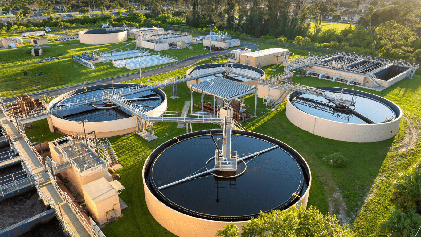 Aerial view of modern water treatment facilities featuring multiple circular basins and advanced infrastructure at a large-scale treatment plant site. These water treatment plants play a critical role in water treatment and wastewater systems, ensuring safe drinking water for the community while meeting federal drinking water standards set by the environmental protection agency (epa). At this plant, water travels through a carefully engineered process that includes aeration, filters, and disinfection to remove contaminants, bacteria, organic matter, and other common form sources of contamination found in contaminated water.  The image highlights two water treatment plants operating within the same site, demonstrating comprehensive management of water systems designed to treat wastewater and protect the environment. Throughout the treatment system, oxygen is introduced during aeration to break down organic matter before treated water is safely prepared for discharge or disposal. These treatment facilities also manage stormwater, helping prevent flood risks and reducing environmental concern caused by high levels of contaminants in local water systems.  Visible pipes connect various facilities within the plant, guiding water through each stage of the process—from initial intake and filtration to final disinfection—ensuring safe drinking water for public use. The infrastructure shown reflects strict adherence to federal drinking water standards and environmental protection agency guidelines, reinforcing the importance of water treatment plants in safeguarding the environment. This modern treatment plant demonstrates how facilities are designed to address contamination at every point, reduce dust and pollutants, and maintain sustainable wastewater systems that protect both the community and surrounding environment.