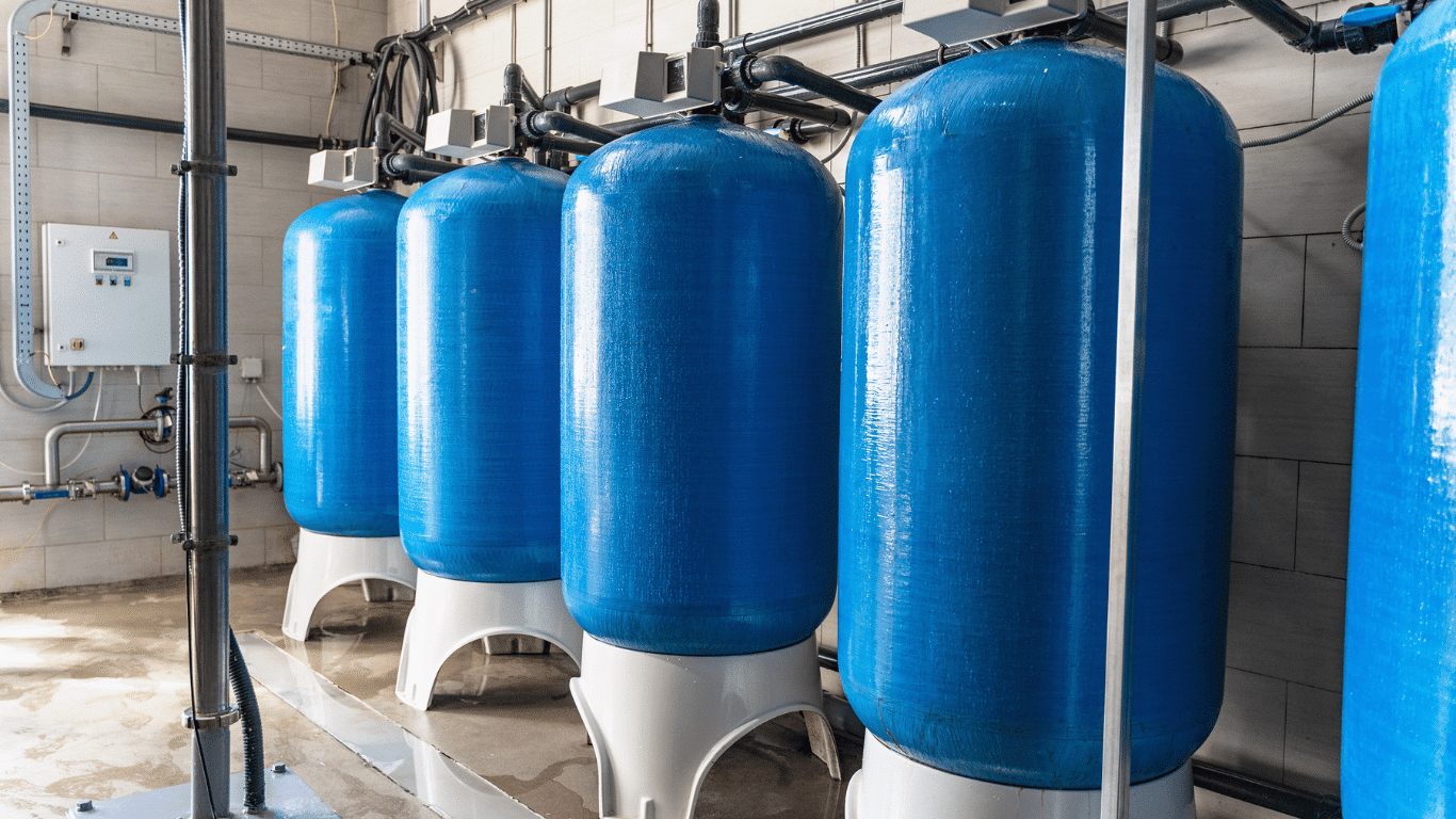 Blue commercial water softener systems with resin tanks and twin tank configuration installed in an industrial water treatment facility for commercial and industrial applications, improving water quality, reducing hard water scale, and producing soft water for boilers, cooling towers, manufacturing equipment, and commercial water systems.