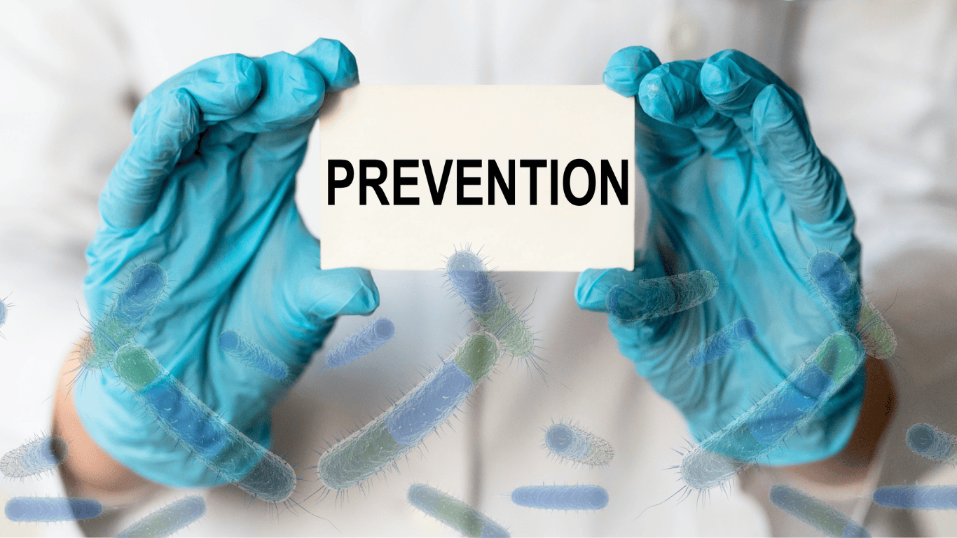 Healthcare worker wearing blue gloves holds a card reading "PREVENTION" against a background with floating bacteria, illustrating strategies for preventing Legionnaires disease in building water systems and potable water systems. The image highlights the importance of water management programs, water management, and proper maintenance of water system components, including water heaters, hot water tanks, water pipes, and the overall plumbing system. Maintaining safe water temperatures in hot and cold water, reducing stagnant water, standing water, and dead legs, preserving disinfectant residual, and performing routine flush procedures help prevent Legionella growth, minimize Legionella growth, reduce Legionella contamination, and lower the risk of Legionella infection caused by bacteria and bacterial growth in contaminated water.
