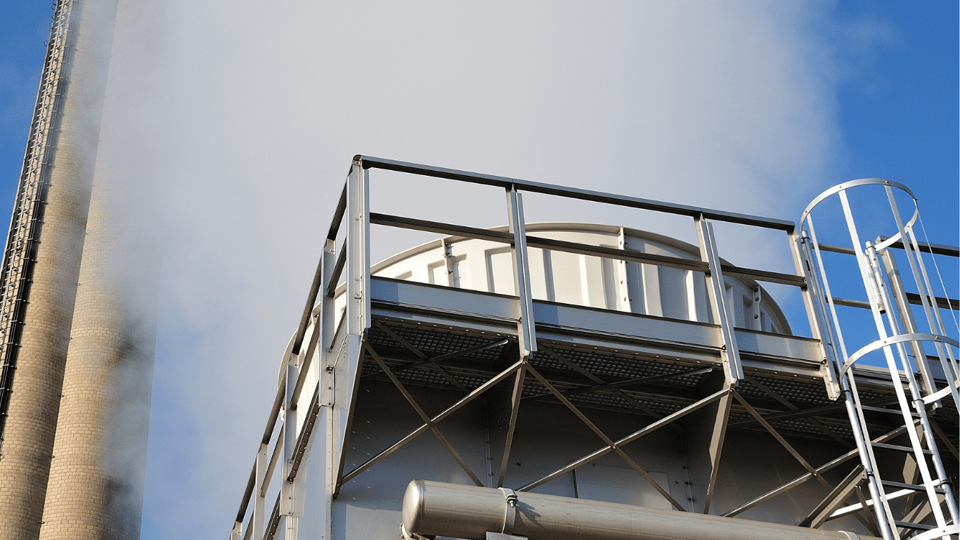 Industrial water cooling tower at a manufacturing facility releasing vapor beside process equipment, supporting industrial water cooling systems with cooling water, heat transfer, temperature control, and system performance.