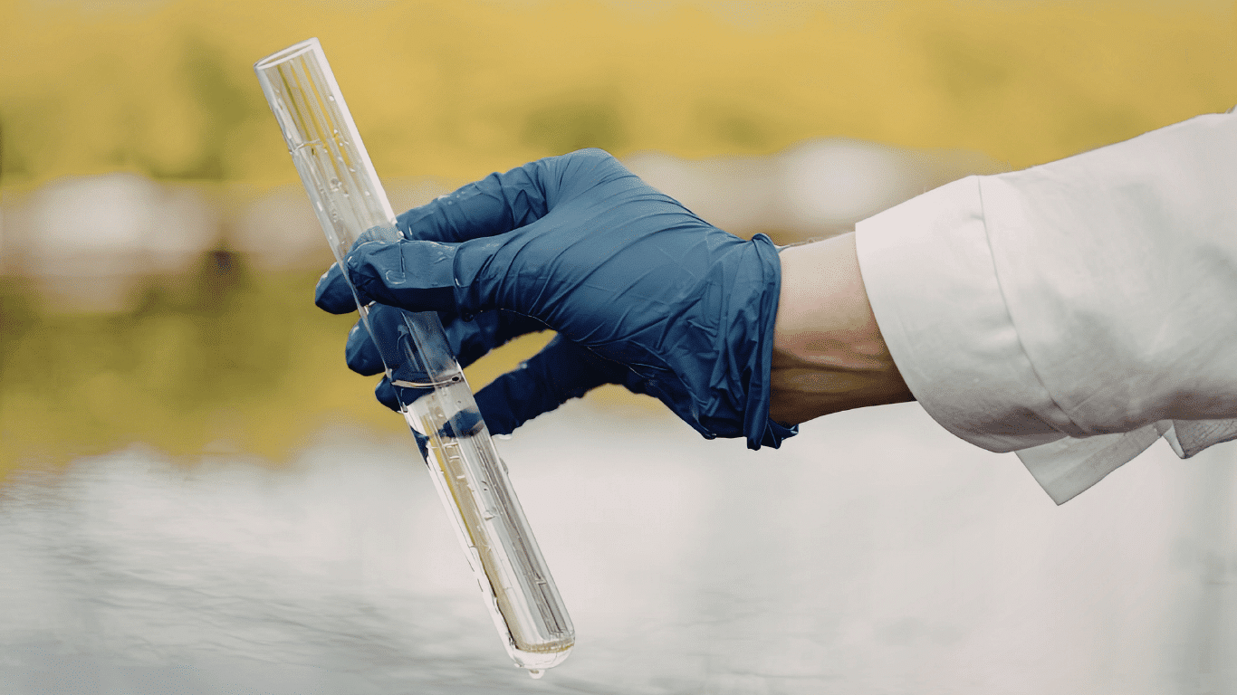 Technician collecting grab samples for water quality monitoring using a laboratory test tube to measure water quality parameters, supporting an online water quality monitoring and water quality monitoring system for real time monitoring, data collection, regulatory compliance, and drinking water quality.
