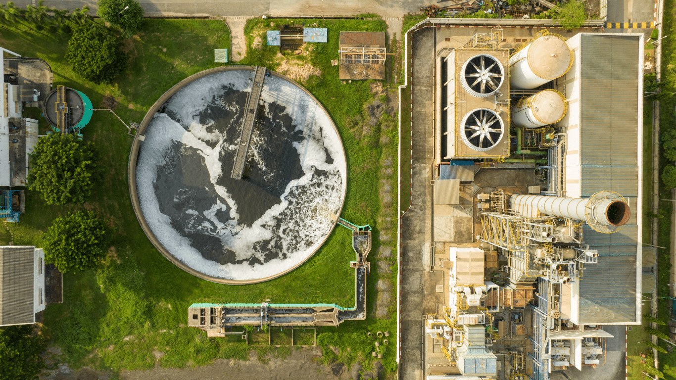 Aerial view of a water treatment plant showing circular treatment tanks, filters, pipes, and an industrial facility where the water treatment process improves water quality. The treatment process removes contaminants, suspended solids, and wastewater through sedimentation, filtration, activated carbon, chemical treatment, disinfection, and chlorine to produce treated water for drinking water and other water treatment applications.
