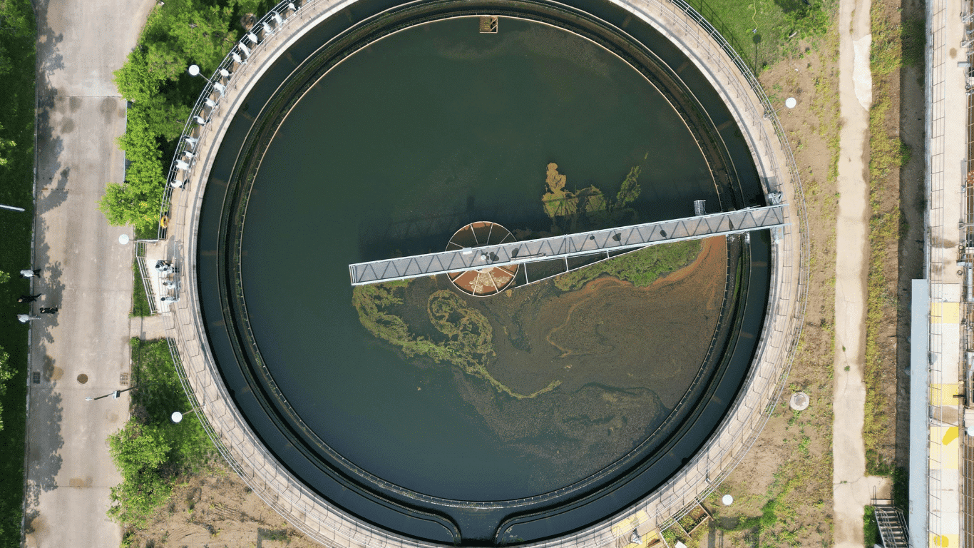 Aerial view of an industrial wastewater treatment plant clarifier showing industrial wastewater undergoing primary treatment and physical separation, with suspended solids settling in a large circular treatment basin.