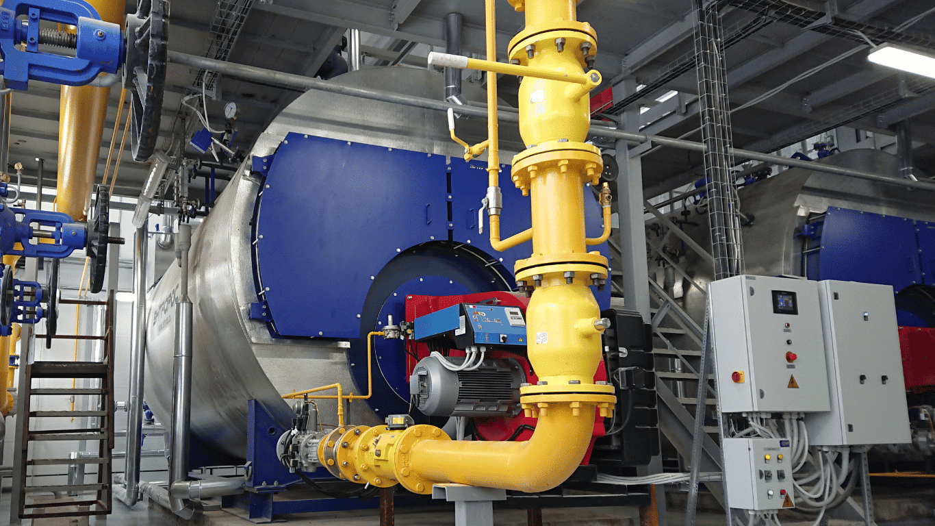 Industrial steam boiler and boiler systems with large pipes, heat exchangers, boiler tubes, control panels, and boiler components inside a manufacturing facility. The image represents industrial boilers used in food processing plants and other steam generating systems, where boiler water, water chemistry, feedwater quality, water quality, heat transfer, heat transfer efficiency, boiler efficiency, thermal efficiency, boiler reliability, system pressure, and operating temperature are carefully managed to support proper operation and extend boiler life.