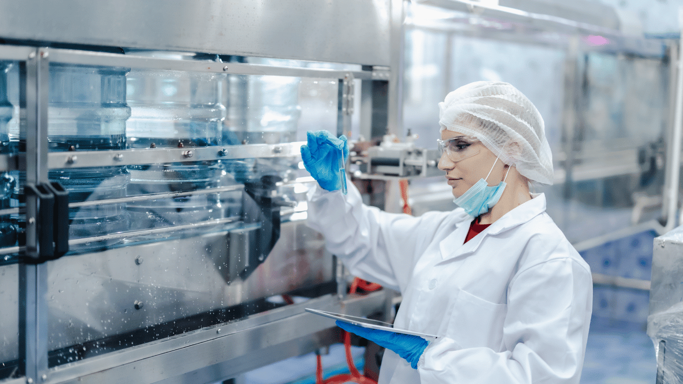 Quality control technician inspecting beverage production equipment while monitoring raw materials and finished product to support food safety, product quality, and consistent production.