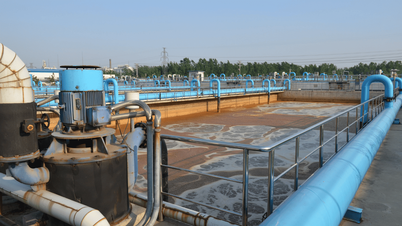 Industrial wastewater treatment basin with blue pipes, mechanical equipment, and foamy water at a water treatment facility.