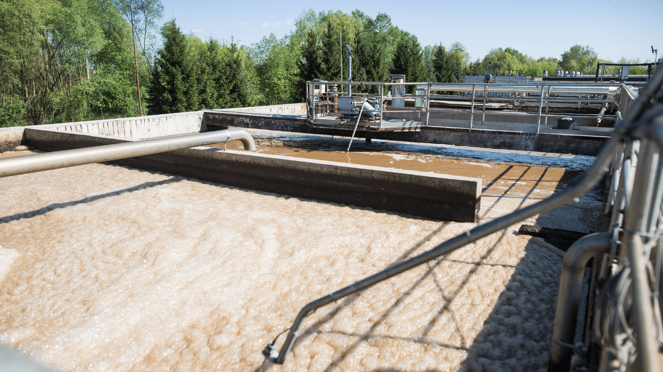 Industrial wastewater treatment basins with foamy water, pipes, and treatment equipment used in pulp and paper wastewater treatment.