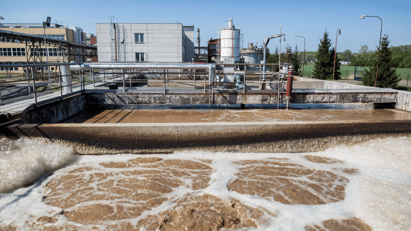 Industrial wastewater treatment facility at an oil refinery, showing treatment basins, pipes, suspended solids, and foamy water during effluent treatment.